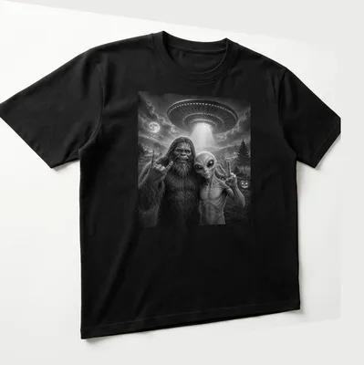 Bigfoot and alien share a selfie with a peace sign in black and white typography — printed on a unisex t-shirt (angled view)