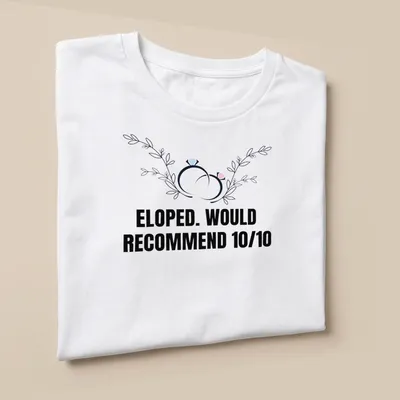 Botanical design featuring wedding rings with the text 'ELOPED. WOULD RECOMMEND 10/10' — printed on a unisex t-shirt (angled view)