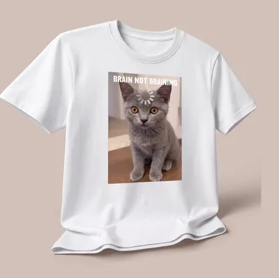 Realistic print of a Chartreux kitten with the text 'BRAIN NOT BRAINING' in gray, orange, and white. — printed on a unisex t-shirt (angled view)