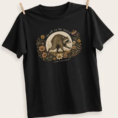 Cottagecore style T-shirt with a whimsical raccoon and the text 'its ok to be weird jimothy from seattle'