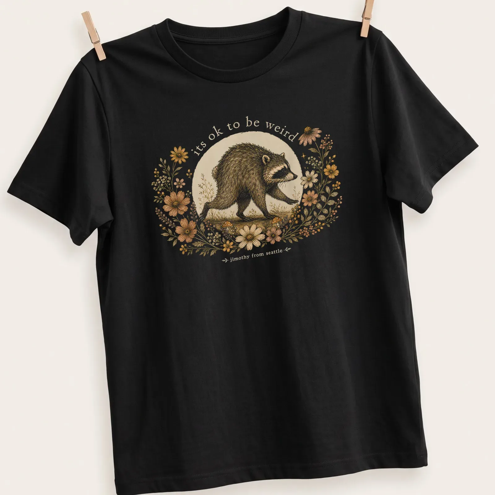 Cottagecore style T-shirt with a whimsical raccoon and the text 'its ok to be weird jimothy from seattle' — printed on a unisex t-shirt