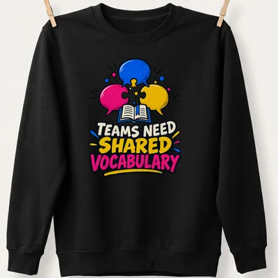 Colorful cartoon graphic with speech bubbles and an open book, stating 'TEAMS NEED SHARED VOCABULARY' — printed on a unisex sweatshirt